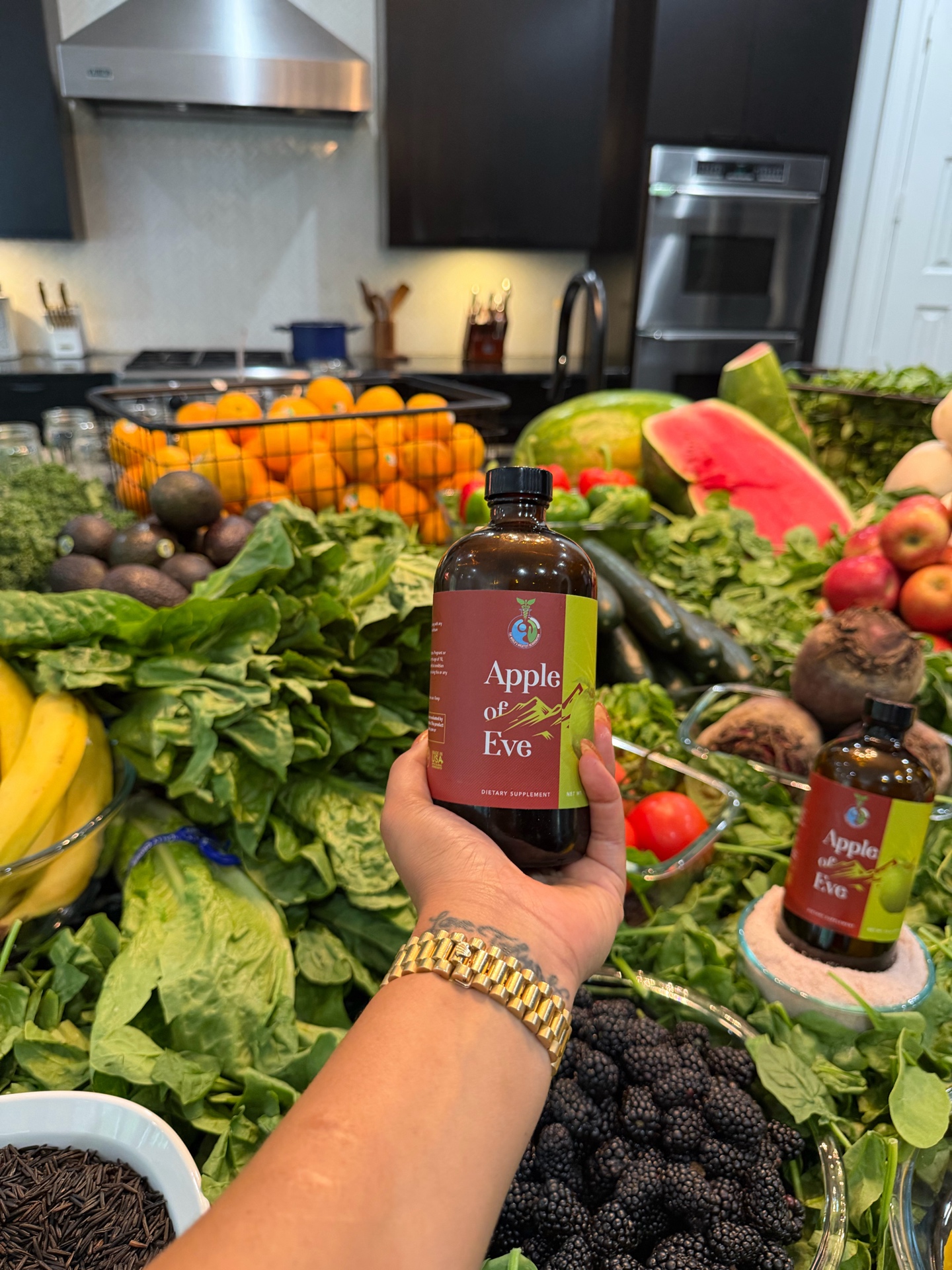 Hand holding an Apple of Eve bottle above leafy greens and fruit